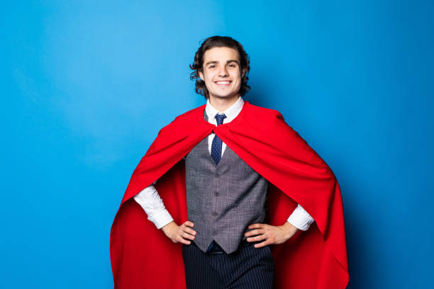 istock Young happy man in red superhero cape over blue background 1212943374
