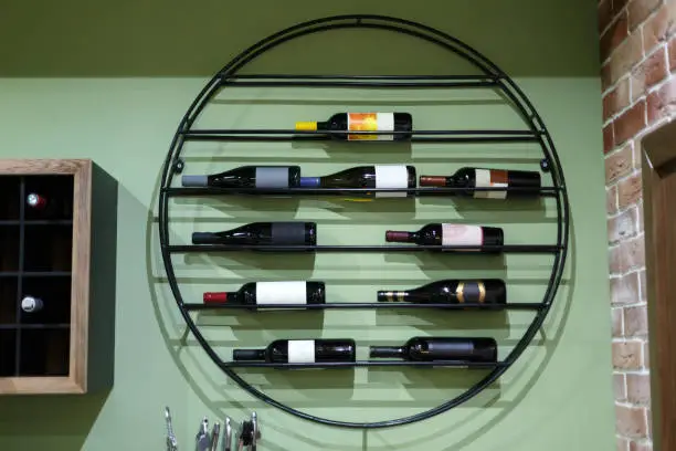 Wine rack with bottles of wine in the interior. A metal shelf in the shape of a circle on which there are several bottles of wine. The color of the wall is green.