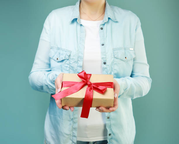 istock Present box in women's hands,gift in paper wrap with red ribbon. 1212952236