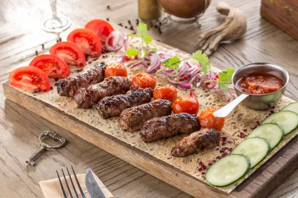 Barbecued kofta kebeb with onion and fresh tomato on lavash bread on wooden table side view
