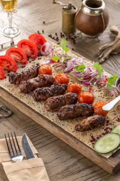 Barbecued kofta kebeb with onion and fresh tomato on lavash bread on wooden table side view