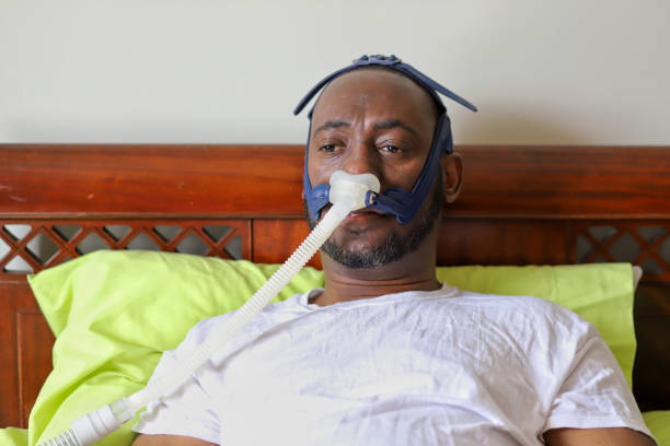 An African-American man wearing cpap mask while laying in bed An African-American man wearing cpap mask while laying in bed sleep apnea photos stock pictures, royalty-free photos & images
