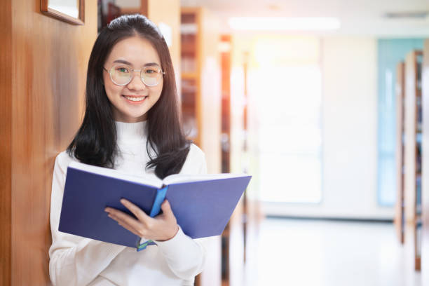 istock Back to school education knowledge college university concept, Beautiful female college student holding her books smiling happily standing in library, Learning and education concept 1212974873