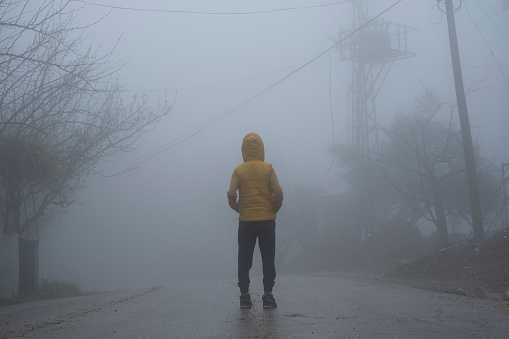 A facing back hoody boy hands in pocket, standing in an abondoned road in air pollution, foggy weather