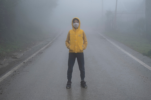 A boy wearing hoody and face mask for protection from virus, is standing and looking to the camera