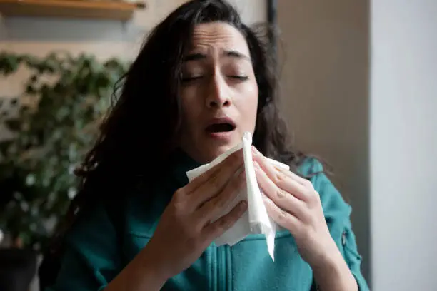 young woman feeling ill and blowing her nose with a tissue