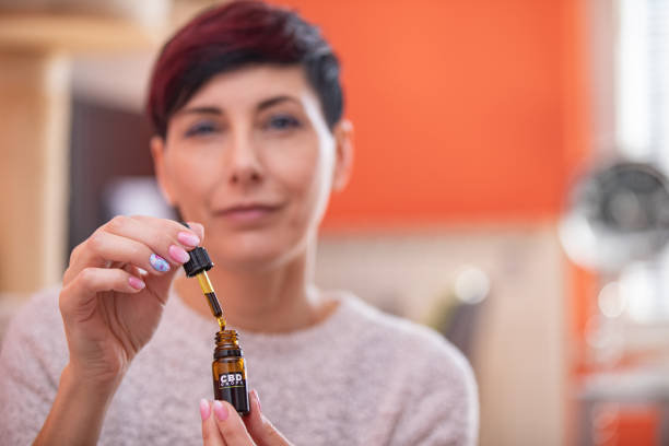 Portrait of Content Adult Woman Holding CBD Oil Drops in Domestic Room Portrait of Content Adult Woman Holding CBD Oil Drops in Domestic Room. cbd oil photos stock pictures, royalty-free photos & images
