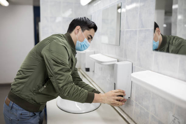 istock Man with a face mask washes his hands in a public bathroom 1212983349