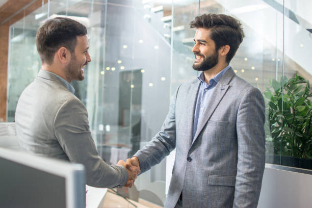 istock Two smiling businessmen shaking hands together while standing in office 1212983427