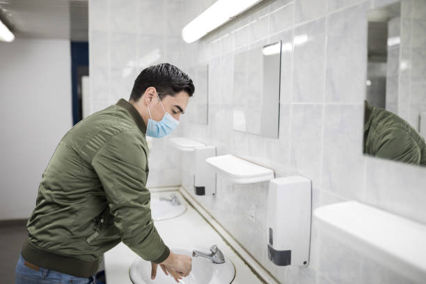 istock Man with a face mask washes his hands in a public bathroom 1212983437