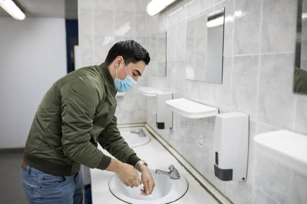istock Man with a face mask washes his hands in a public bathroom 1212983488