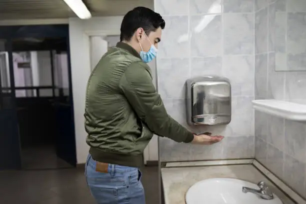 Concept, diseases, viruses, allergies, air pollution. Portrait of a young man wearing a protective mask and washing his hands in a public bathroom. The face of a young man wearing a mask to prevent germs, toxic fumes and dust. Prevention of bacterial infection with Corone virus or Covid 19 in the air around streets and gardens.