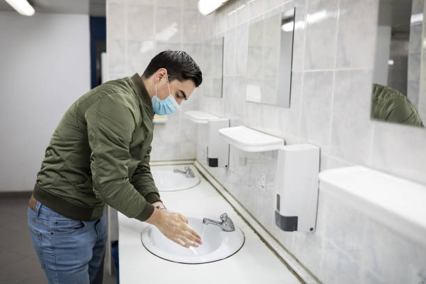 homem com máscara facial lava as mãos em um banheiro público - one person sink washing hands bathroom - fotografias e filmes do acervo