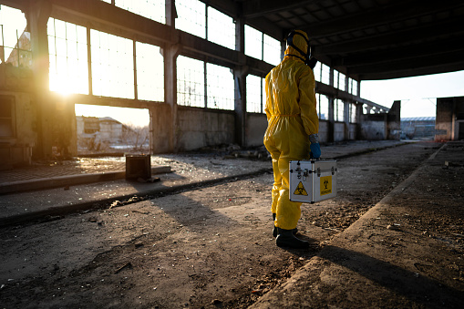 Man in protective workwear examining radioactive ruined building.
