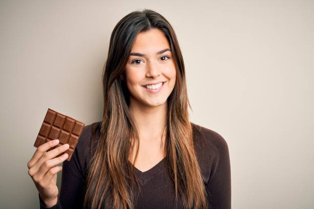 junge schöne mädchen hält süße bar schokolade über isolierten weißen hintergrund mit einem glücklichen gesicht stehen und lächelnd mit einem selbstbewussten lächeln zeigt zähne - toothy smile relaxation white healthcare and medicine stock-fotos und bilder