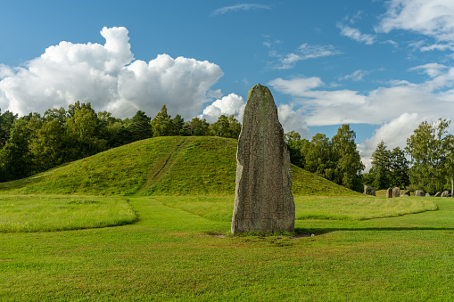 Large rune stone at an old burial ground in Anundshog in Sweden. In summer sunlight, lush foliage and a blue sky