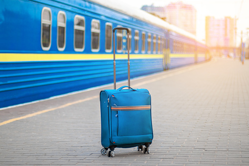 Train station and blue carry-on suitcase with metal handle on the platform. In the background, train cars tend to distance. Empty platform, epidemic, suspension of railway traffic