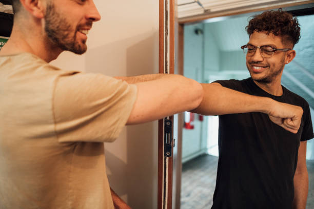 Alternative Handshake Mixed race male using an elbow bump as an alternative handshake on his Caucasian male work colleague in the office. office buddies stock pictures, royalty-free photos & images