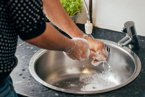 Soapy Hands Close up image of a Mixed race male washing the soap off his hands whilst standing over a small kitchen sink at work water sanitation worker washing faucet stock pictures, royalty-free photos & images