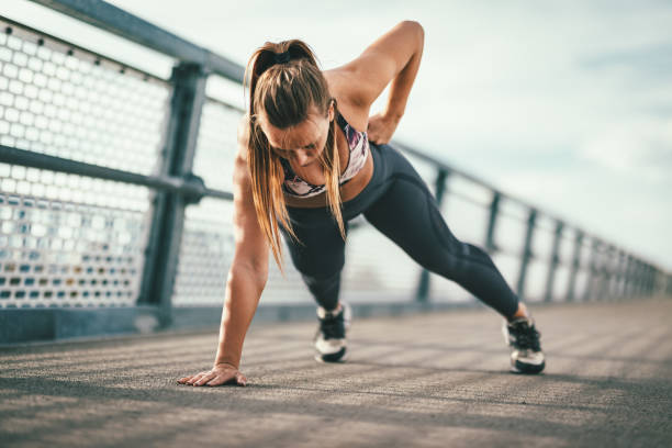 So Many Benefits Of Outdoors Exercise Young female runner doing push-upos exercise on a river bridge, preparing for morning workout. bodyweight training stock pictures, royalty-free photos & images