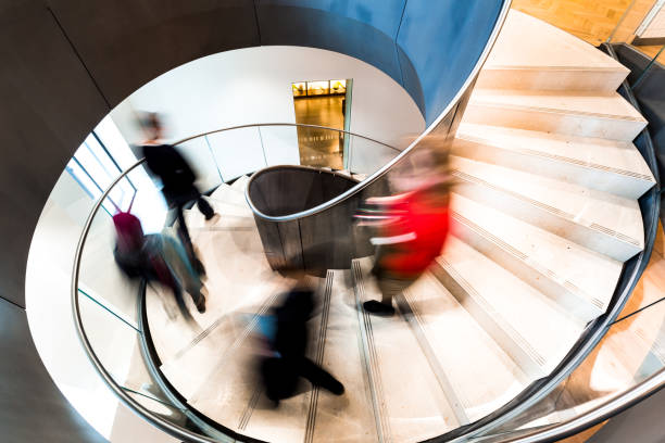 blurred motion of urban people running down futuristic modern spiral staircase - office time lapse imagens e fotografias de stock