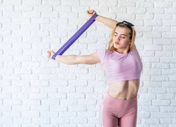 istock Athletic woman doing exercises using a resistance band at home at white brick wall background 1213002068