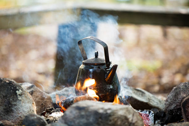 Man and woman making coffee in big kettle on campfire