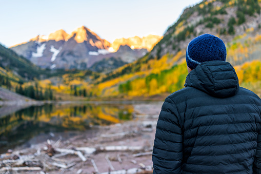 Maroon Bells lake at sunrise with man looking in Aspen, Colorado with rocky mountain peak in October 2019 autumn and vibrant trees reflection on water