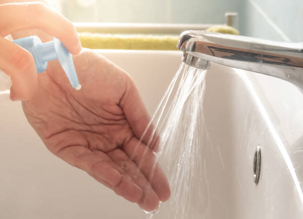 istock Person sprays liquid soap on his hands before washing himself whit sink. 1213008820