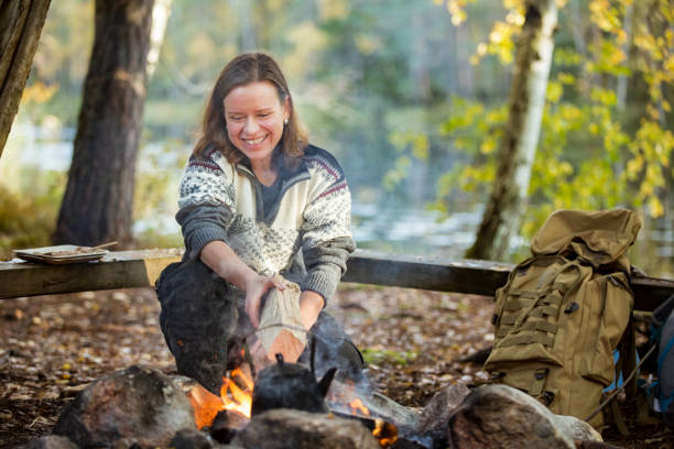 Man and woman making coffee in big kettle on campfire