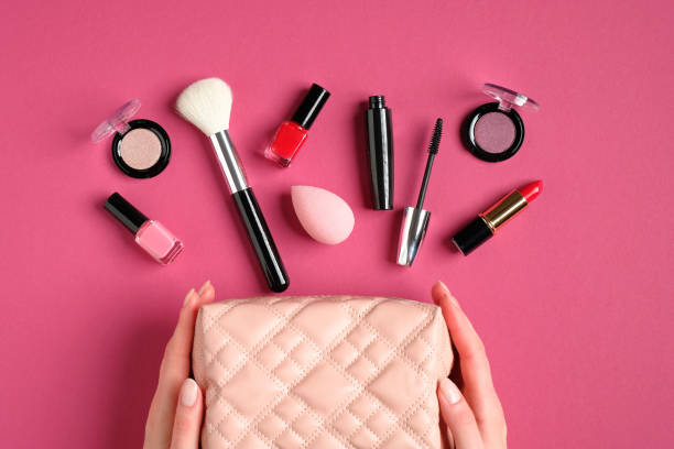 manos femeninas sosteniendo bolsa de maquillaje con productos cosméticos sobre fondo rosa. plano, vista superior. concepto de belleza y moda. - cosmetic bag fotografías e imágenes de stock