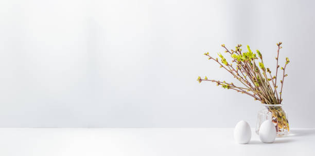 istock Home interior with easter decor. Green buds on branches in a glass vase, easter eggs on a light background 1213009553