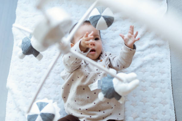 uma menina bonita está assistindo e brincando com o brinquedo móvel musical das crianças em casa. - using mobile - fotografias e filmes do acervo