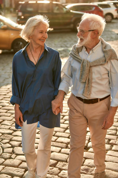 istock Active weekend. Elderly couple holding hands and looking to each other with smile while walking together through the street 1213017641