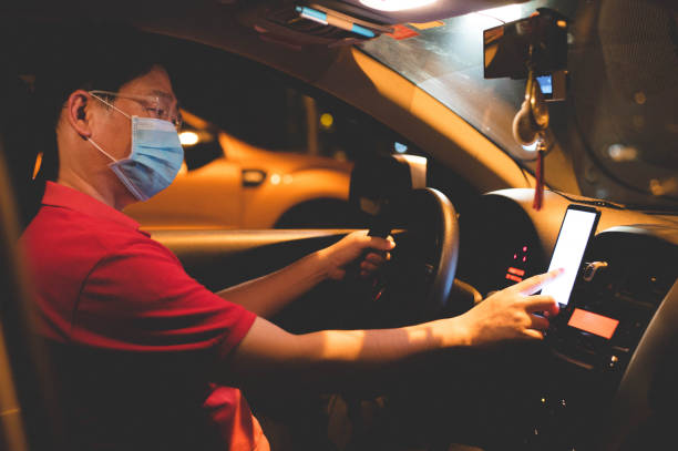 Asian male E-hailing driver with face mask using smartphone Image of Asian male E-hailing driver with face mask using smartphone to received order. taxi driver photos stock pictures, royalty-free photos & images