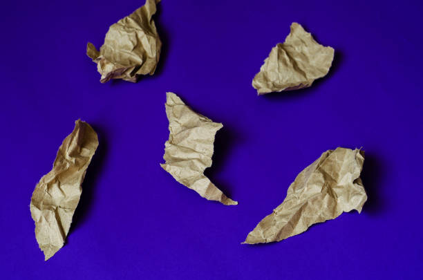 Blue background with pieces of brown paper. Five crumpled pieces of paper with torn edges. Abstract background. Top view at an angle. Selective focus. Close-up.