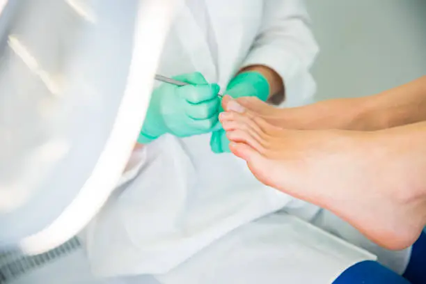 Woman sitting in chair, having foot treatment in spa salon.  Professional medical pedicure specialist in protective mask using special electric lathe and tools.