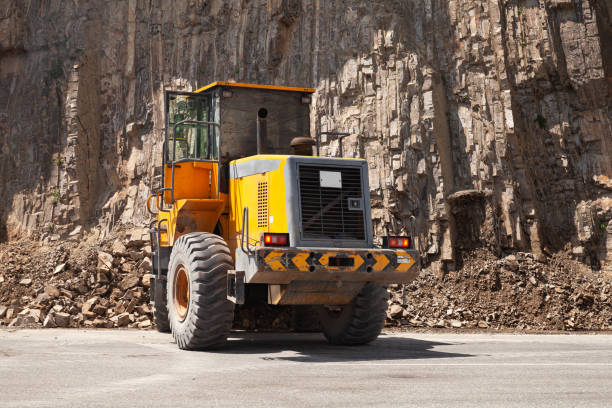 Yellow tractor clears a mountain road from rocks
