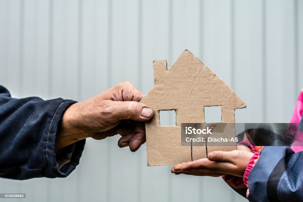 paper house A man's hand holds a paper house cut out of cardboard. Nearby, children's hands hold the house from below. Homelessness Stock Photo