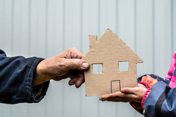 paper house A man's hand holds a paper house cut out of cardboard. Nearby, children's hands hold the house from below. begging social issue stock pictures, royalty-free photos & images