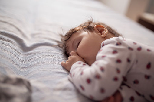 Young baby girl sleeping while sucking thumb on a bed