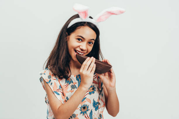 dolce bambina che indossa orecchie da coniglietto che mangiano uovo di pasqua al cioccolato. pasqua in brasile - easter easter egg child chocolate foto e immagini stock