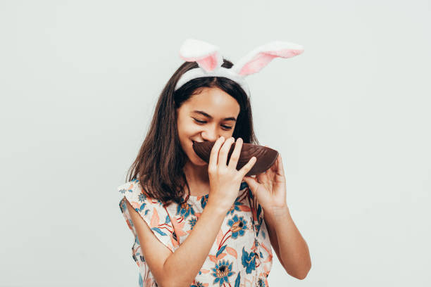 dolce bambina che indossa orecchie da coniglietto che mangiano uovo di pasqua al cioccolato. pasqua in brasile - easter easter egg child chocolate foto e immagini stock