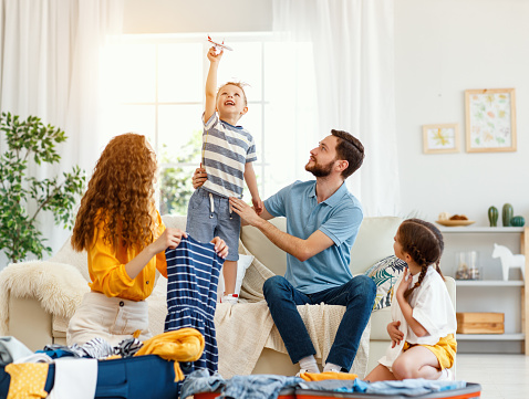 Happy family of parents and boy with girl packing suitcases for vacation trip while playing on sofa in living room