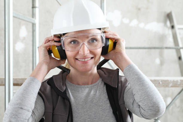 portrait de femme de travail souriant utilisant le casque, les lunettes de sécurité et les écouteurs de protection d’audition, fond intérieur de chantier d’échafaudage - ear muff photos et images de collection