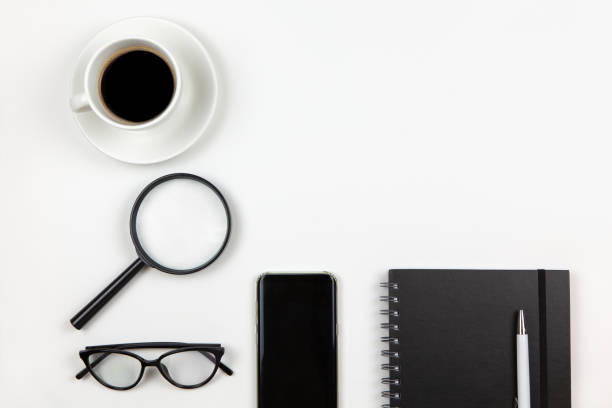 istock Modern unisex working space, top view. Notepad, pen, coffee, smartphone, magnifier, glasses on white background, copy space, flat lay. Desktop of freelancer. Work from home concept. Monochrome image 1213050633