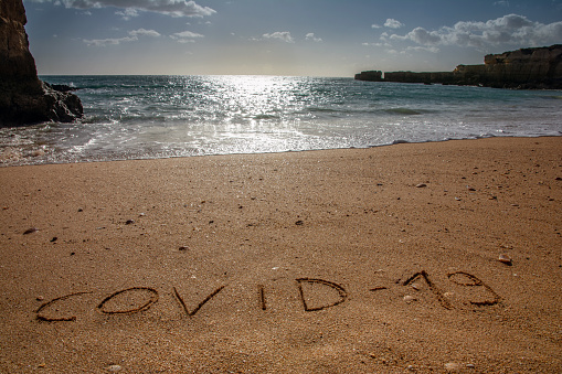Travel and tourism concept for pandemic alert, flights and trips cancellation.  Text written on the sandy beach in Algarve.