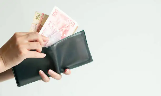 Close-up of the hands holding a short wallet and another hand bring 2 banknotes of Hong Kong money that have value 100 Dollar Hong Kong (HKD) out of the wallet.