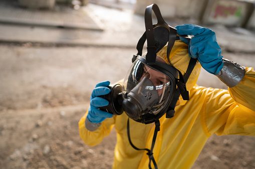 Man in protective workwear at the place of a hazardous accident putting on a gas mask.