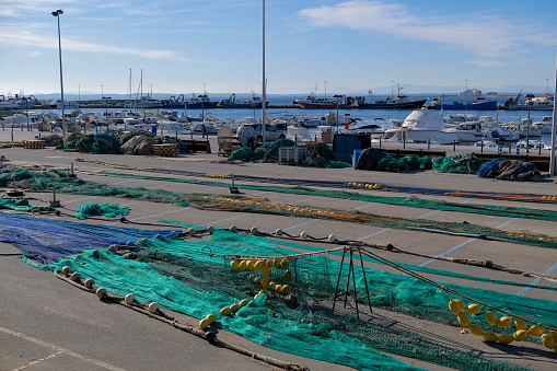 View on the fishing gear and equipment on boats in the port background. Lay out various fishing nets, bobbers, mooring line, floats. Preparing to sail, fishing. Drying and repairing nets on the dock.